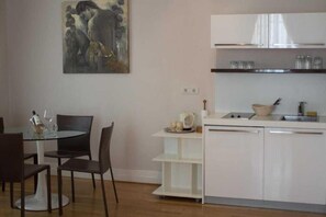 Une cuisine moderne avec des meubles blancs, une table à manger en verre et un tableau accroché au mur.