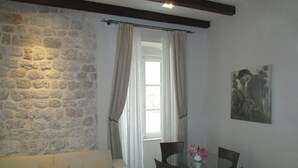A room with a stone wall, a white sofa, a glass table with chairs, and a painting on the wall. - Olea (Dubrovnik)