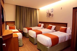 A hotel room with three beds, each with white and orange bedding, a wooden headboard, and a wooden desk. - Al Bostan Al Masi Hotel (Makkah)