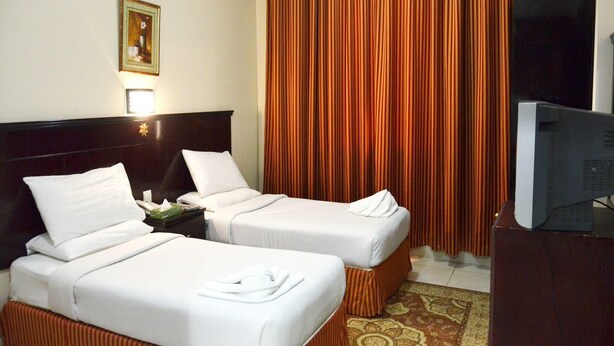 A hotel room with two beds, a television, and a large window with curtains. - Al Bostan Al Masi Hotel (Makkah)