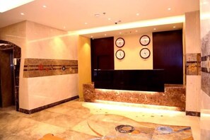 A lobby with a reception desk, clocks on the wall, and a marble floor. - Al Bostan Al Masi Hotel (Makkah)