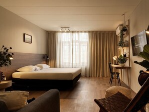 Ein Hotelzimmer mit Bett, Schreibtisch, Stuhl, Fernseher und Pflanze.
