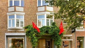 A brick building with large windows and a wooden door. There are two red flags on the building. - St. Martenslane Hotel Maastricht (Maastricht)