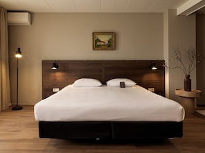A modern hotel room with a large bed, two bedside lamps, a painting on the wall, and a vase with branches on a side table. - St. Martenslane Hotel Maastricht (Maastricht)