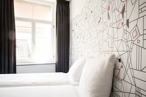 A hotel room with a large window, a bed with white bedding, and a wall with a geometric pattern. - Mabi Hotel Centrum (Maastricht)