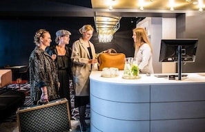 A reception area with a curved counter, a television, and a chandelier. - Mabi Hotel Centrum (Maastricht)