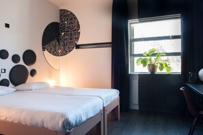 A modern bedroom with a bed, a wall art piece, a potted plant, and a window with curtains. - Mabi Hotel Centrum (Maastricht)