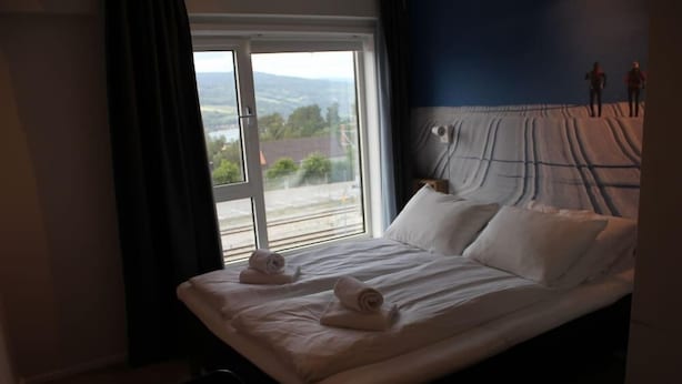 A hotel room with a large bed, two pillows, and two rolled towels. There is a window with a view of a landscape. - Lillehammer Station Hotel & Hostel (Lillehammer)