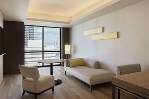 A modern living room with a sofa, armchair, and dining table, large windows with a city view, and minimalist decor. - Courtyard BY Marriott Osaka Honmachi (Osaka)