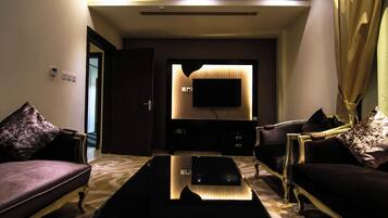 A modern living room with a flat-screen TV mounted on a wall, two sofas with cushions, a coffee table, and a patterned carpet.