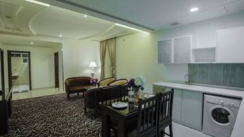 A hotel room with a dining area, a kitchen with a washing machine, and a bathroom with a shower and toilet.