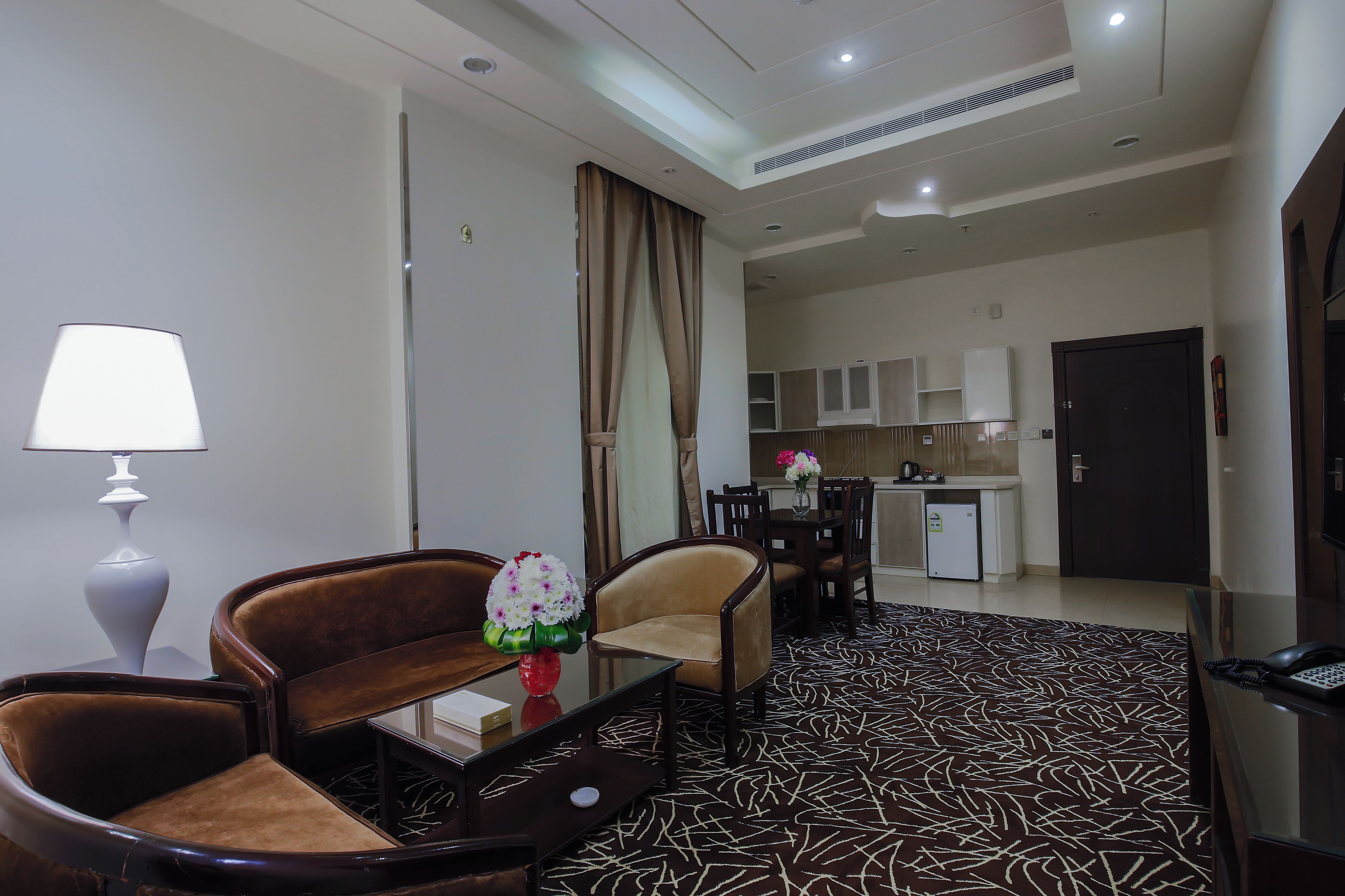 A hotel room with a sofa, armchair, coffee table, lamp, and a patterned carpet.