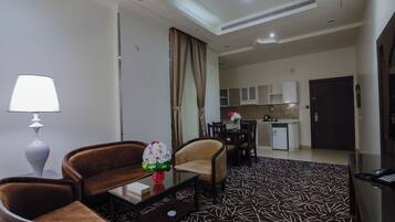 A hotel room with a sofa, armchair, coffee table, lamp, and a patterned carpet.
