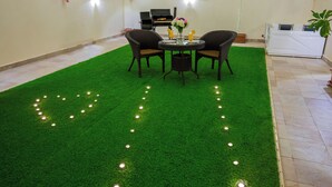 A room with a green artificial turf floor, a round table with chairs, a grill, and a white washing machine. - Rest Night Hotel Suites Al Hamra (Riyadh)