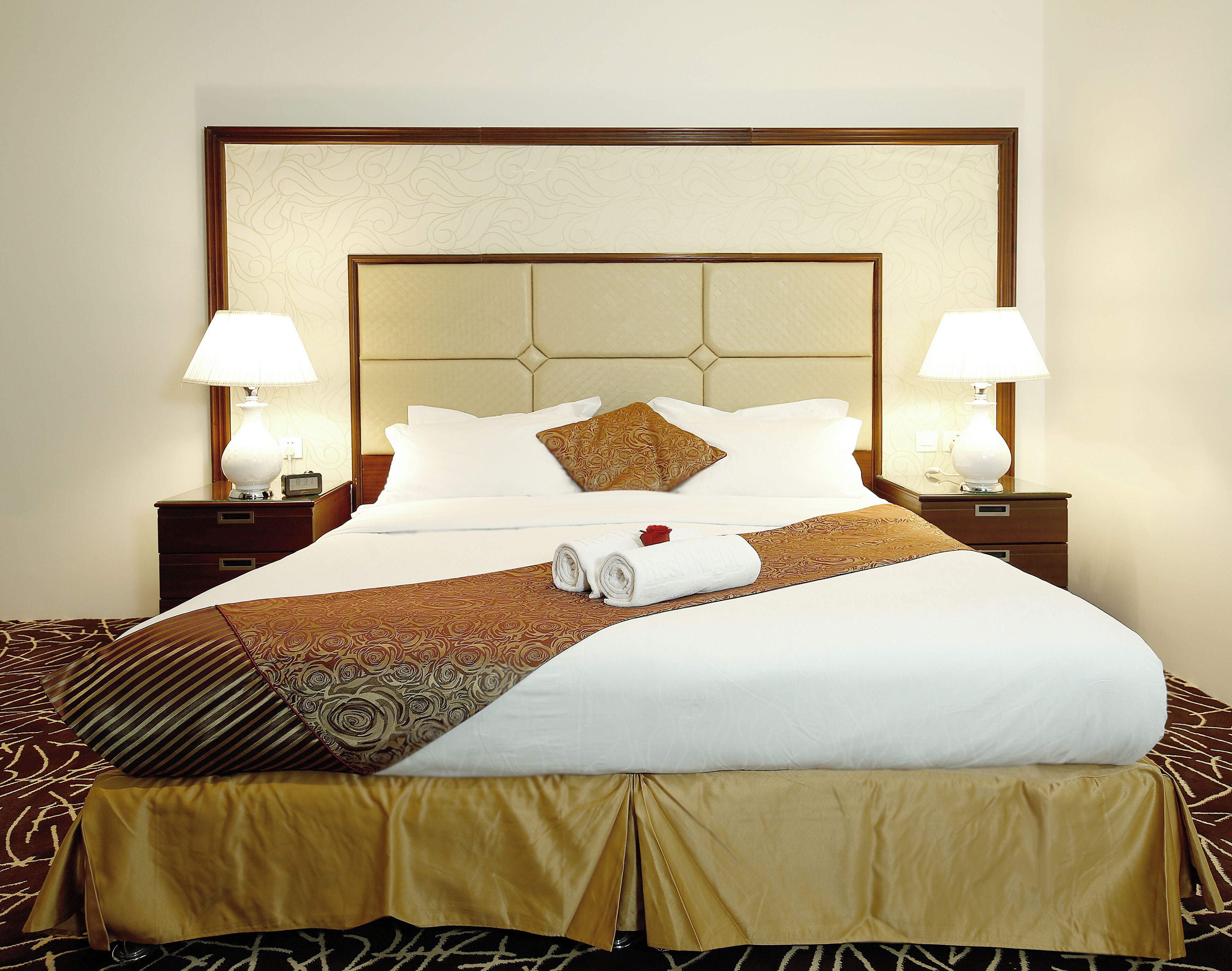 A neatly made bed with a patterned bedspread, two bedside lamps, and a decorative headboard.