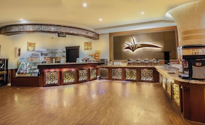 A coffee shop with a curved counter, a coffee machine, and various coffee cups and pastries. - Rest Night Hotel Suites Al Hamra (Riyadh)