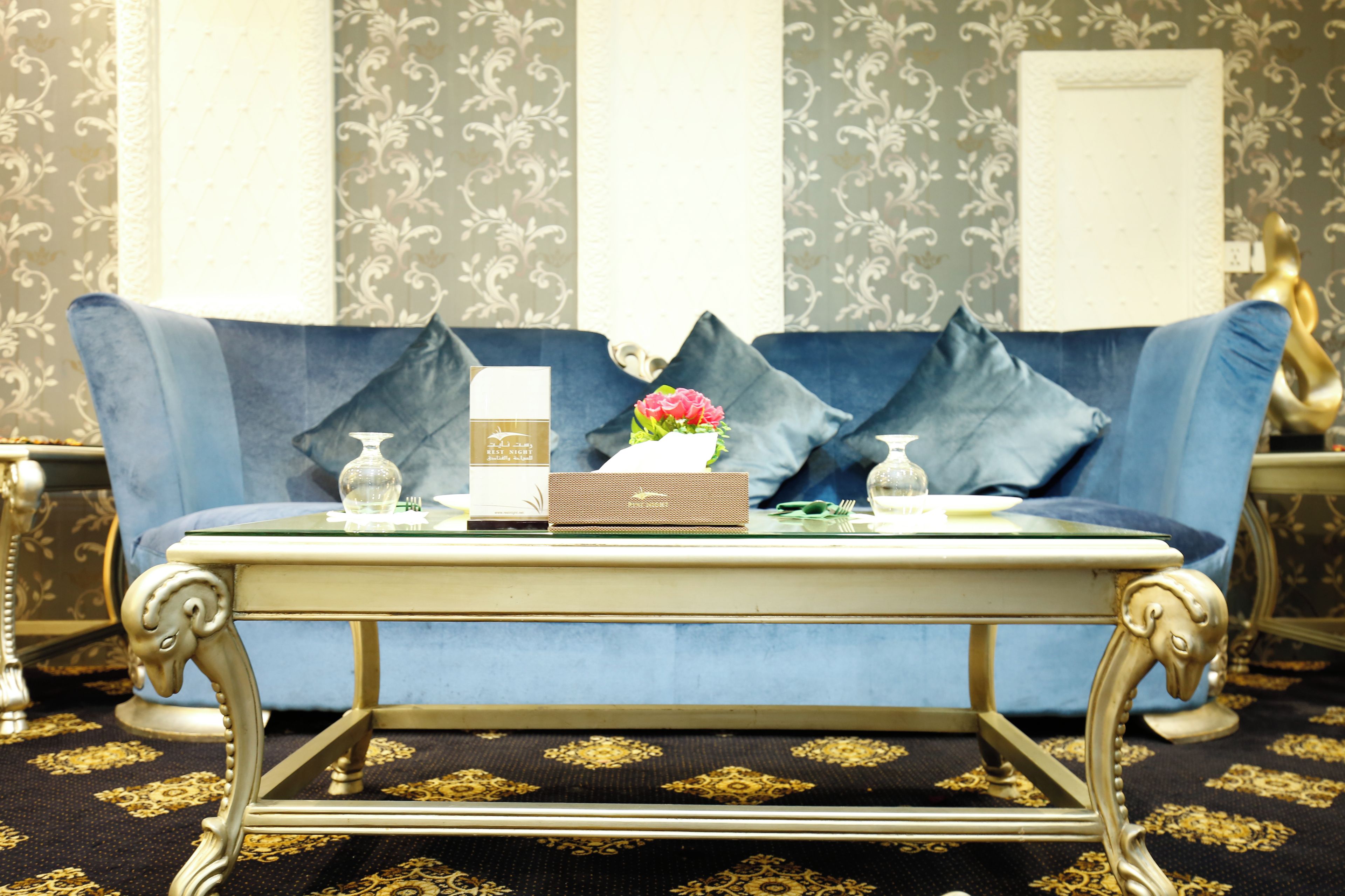 A blue sofa with decorative pillows, a small table with a vase of flowers, and a box on the table.