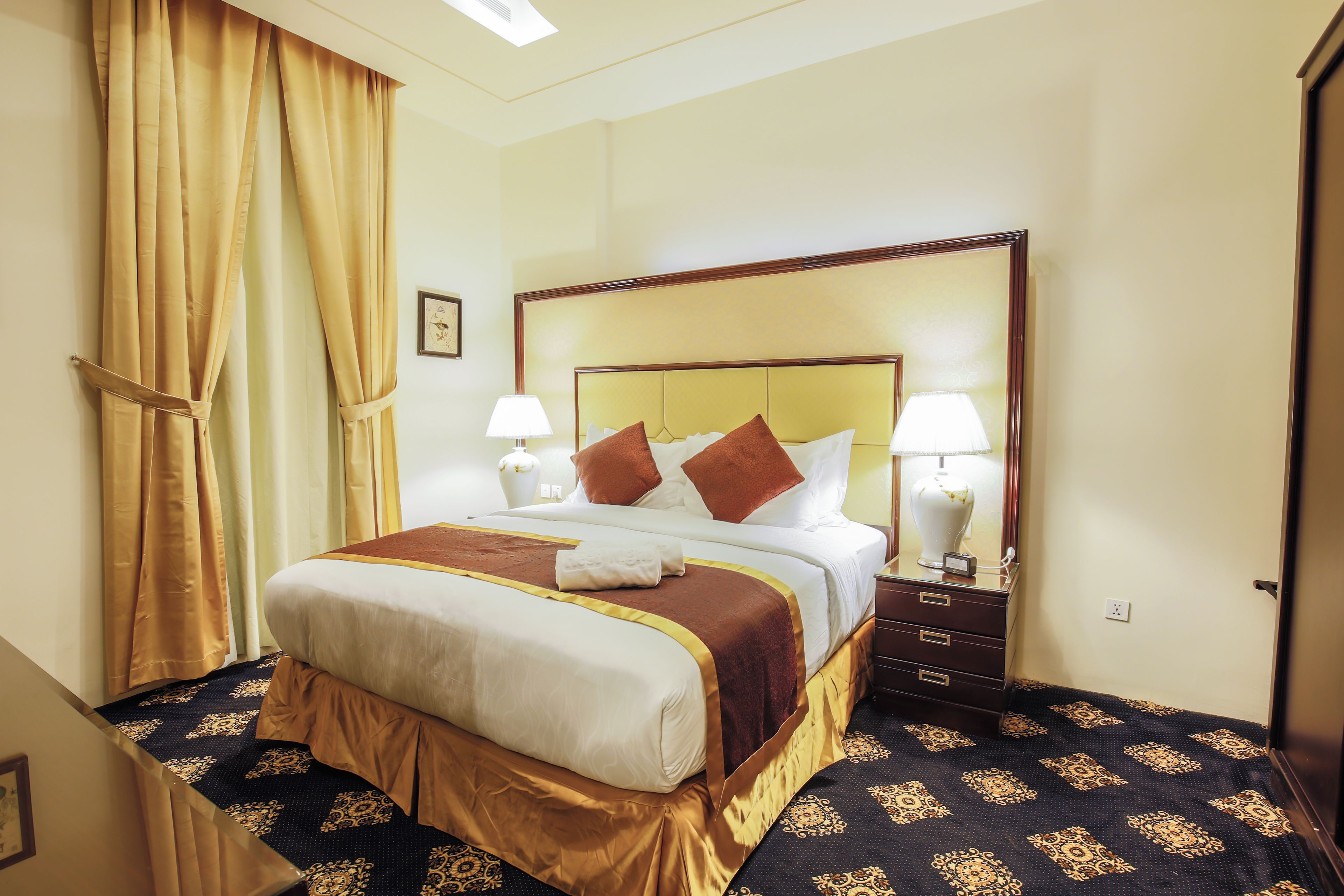 A hotel room with a large bed, two bedside tables with lamps, a wooden headboard, and a patterned carpet.