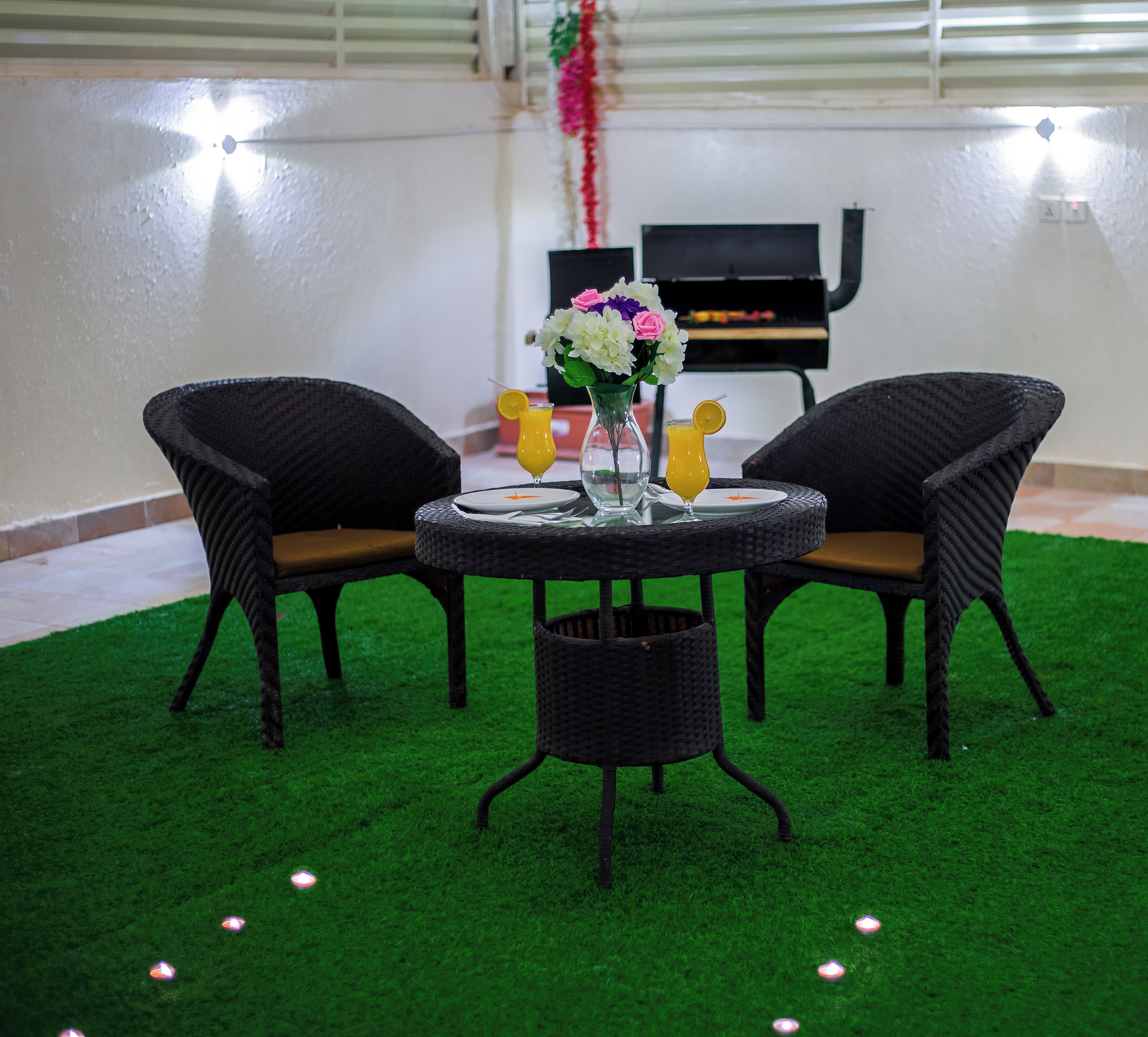 A dining area with a round table, two chairs, a vase with flowers, and a glass of orange juice.