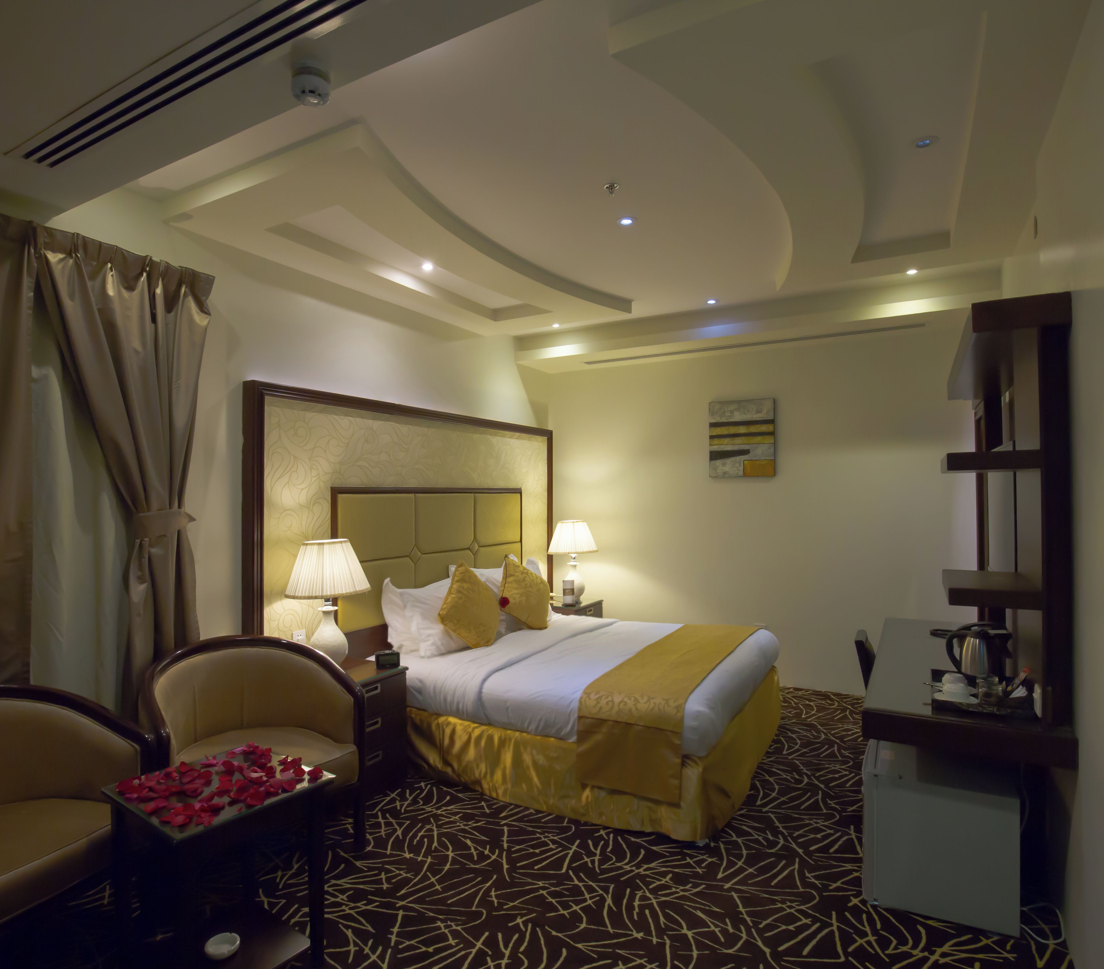 A hotel room with a bed, a chair, a desk with a coffee maker, and a wall-mounted TV.