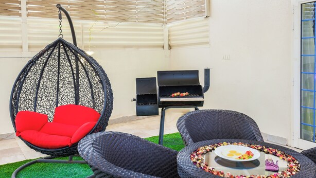 A patio area with wicker furniture, a hanging chair, and a grill. - Rest Night Hotel Suites Al Hamra (Riyadh)