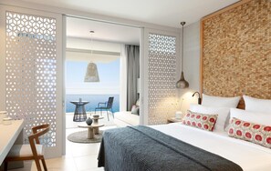 Une chambre d’hôtel comprenant un lit, un coin repas, un balcon avec vue sur la mer et un mur décoratif.