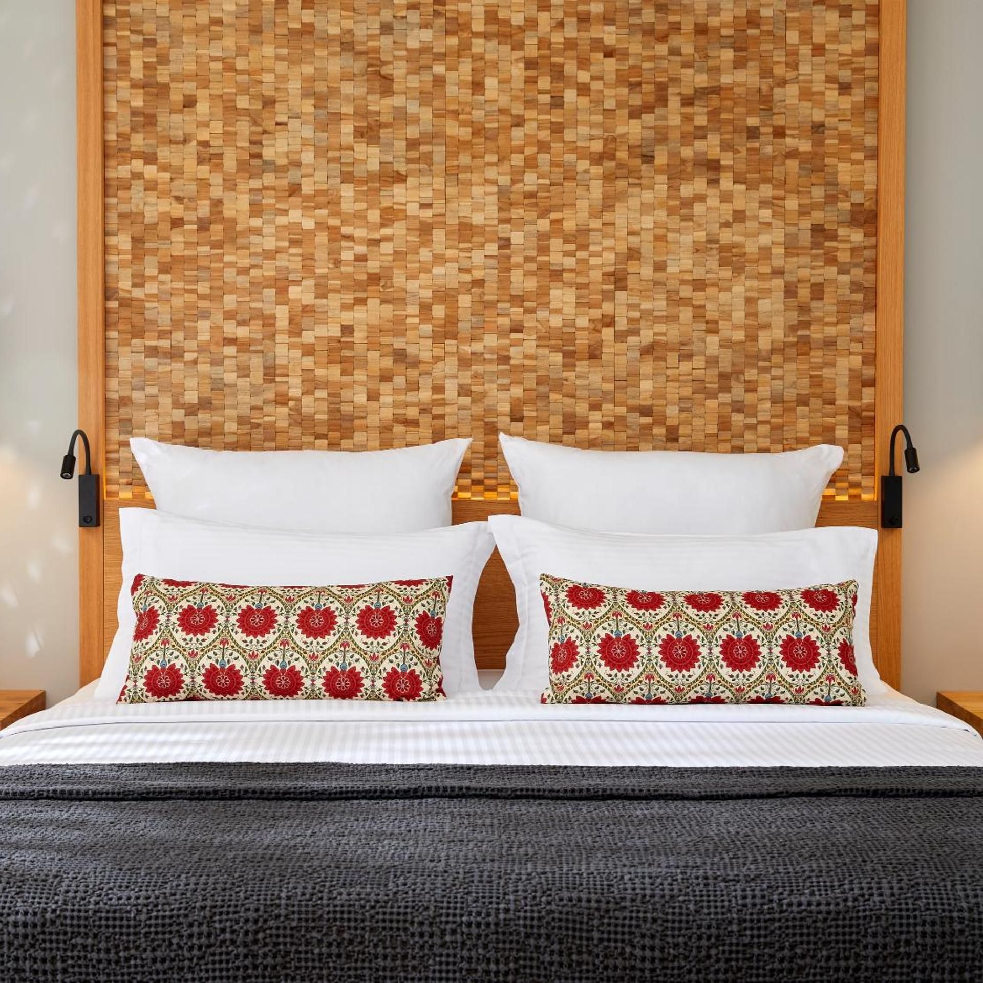 A bed with white bedding and two decorative pillows with a red and beige pattern.