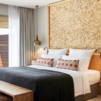 Un dormitorio con cama, almohadas, una mesita de noche, una lámpara colgante y un panel de pared tejido.