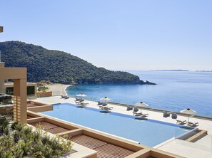A resort pool with lounge chairs and umbrellas, overlooking a beach and sea. - Marbella Elix (Igoumenitsa)
