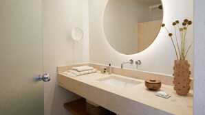A bathroom with a large oval mirror, a sink with a beige countertop, a small round mirror, and a vase with dried flowers. - Marbella Elix (Igoumenitsa)