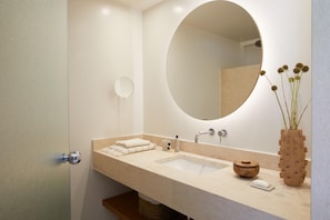 A bathroom with a large oval mirror, a sink with a beige countertop, a small round mirror, and a vase with dried flowers. - Marbella Elix (Igoumenitsa)
