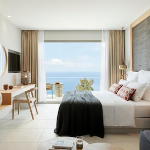 A modern bedroom with a bed, a desk, a chair, a TV, and a view of the sea. - Marbella Elix (Igoumenitsa)