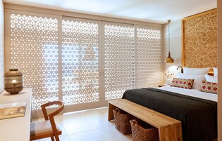 Un dormitorio con cama, un banco de madera, una silla, una mesita de noche y un adorno en la pared.