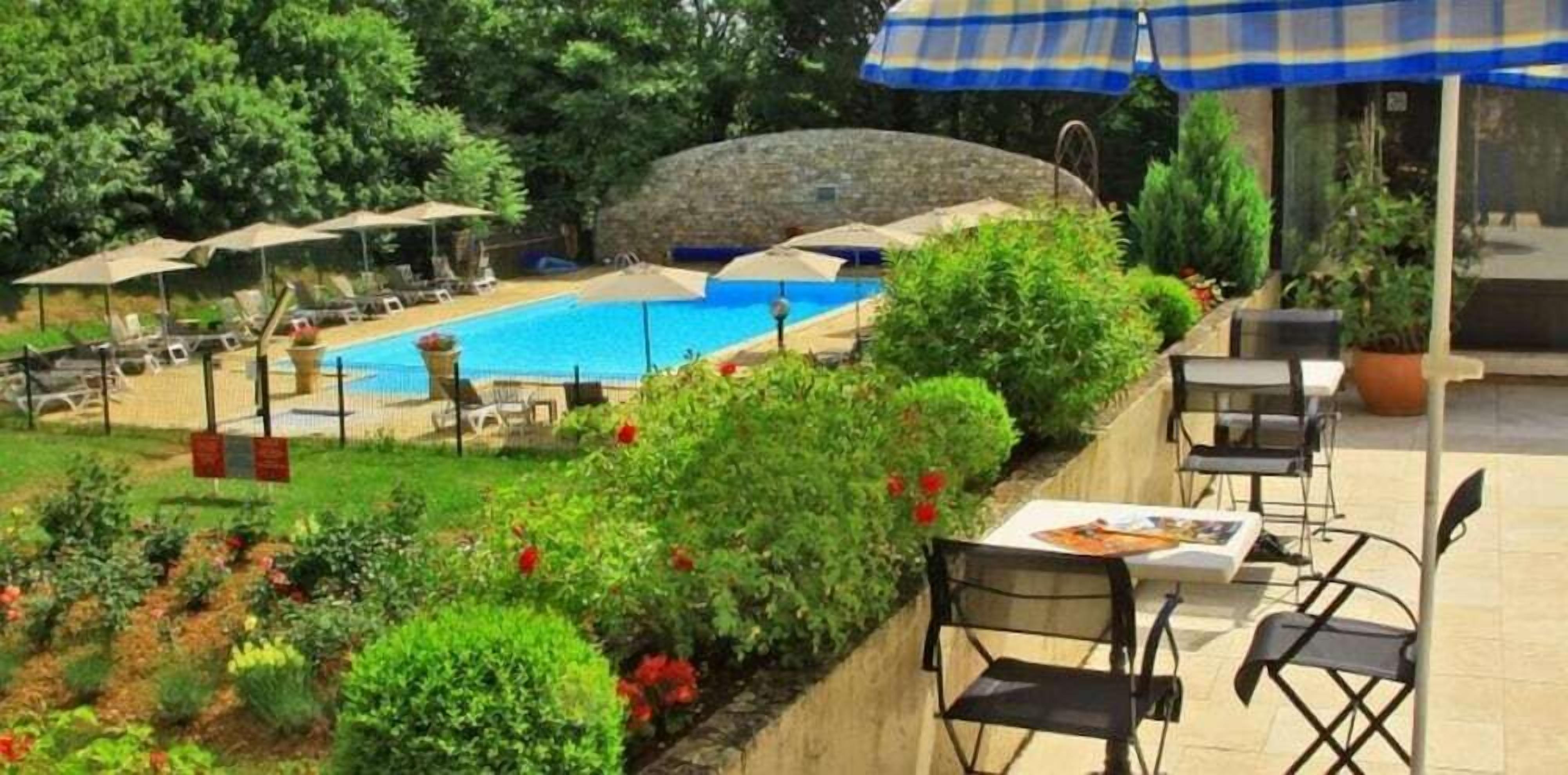 A pool area with lounge chairs and umbrellas, surrounded by greenery and a stone wall.