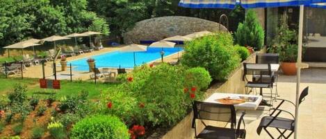 A pool area with lounge chairs and umbrellas, surrounded by greenery and a stone wall.