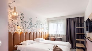 A hotel room with a bed, a desk, a chair, a TV, and a bookshelf. - Ibis Pontivy (Pontivy)