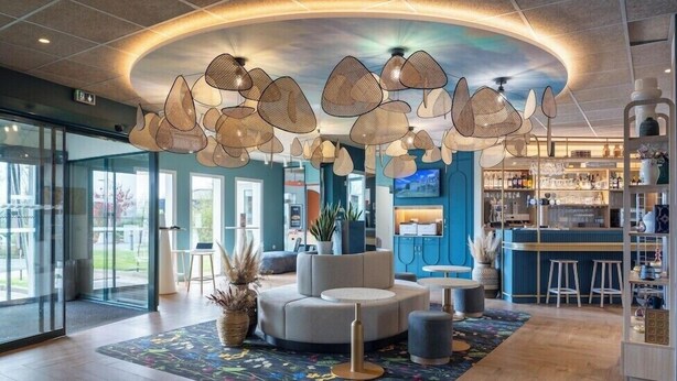 A modern lobby with a central seating area, a bar, and a large window providing a view of the outdoors. - Ibis Pontivy (Pontivy)