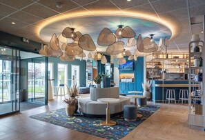 En moderne lobby med et centralt siddeområde, en bar og et stort vindue med udsigt udendørs.