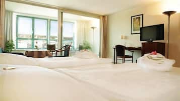 A hotel room with two beds, a desk, a chair, a television, and a large window with a view.