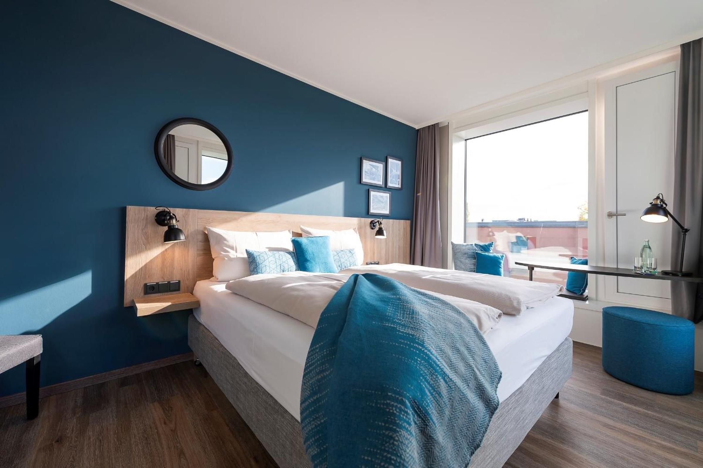 A modern hotel room with a large bed, a bedside table, a desk, and a view of the outdoors.