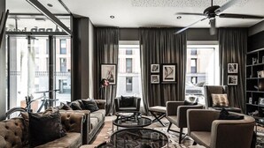 A modern living room with a sofa, armchairs, and a coffee table. There are large windows with curtains, a ceiling fan, and a bookshelf. - Harbr Hotel Konstanz (Konstanz)