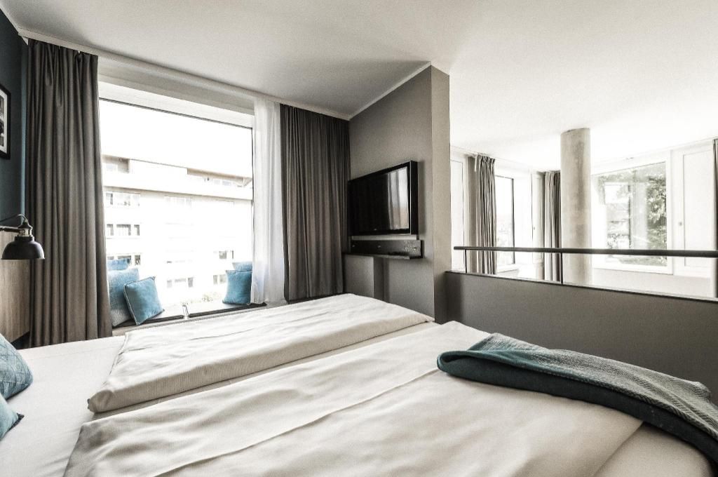 A hotel room with two beds, a TV mounted on the wall, and a window with curtains.