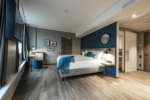 A modern bedroom with a large bed, bedside tables, a small desk, and a round mirror on the wall. - Harbr Hotel Konstanz (Konstanz)