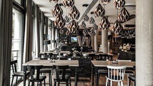 A modern restaurant interior with geometric pendant lighting, wooden tables, and black and white chairs. - Harbr Hotel Konstanz (Konstanz)