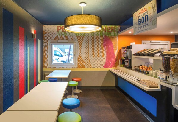A restaurant with a counter, stools, and a window with a view. - B&B Hotel Cergy Pierrelaye (Pierrelaye)