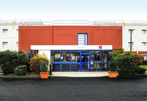 A building with a red facade, blue-framed windows, and a door. - B&B Hotel Cergy Pierrelaye (Pierrelaye)