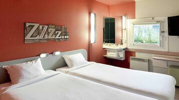 Quarto de hotel com duas camas, banheiro com espelho e pia, e janela com vista para árvores.