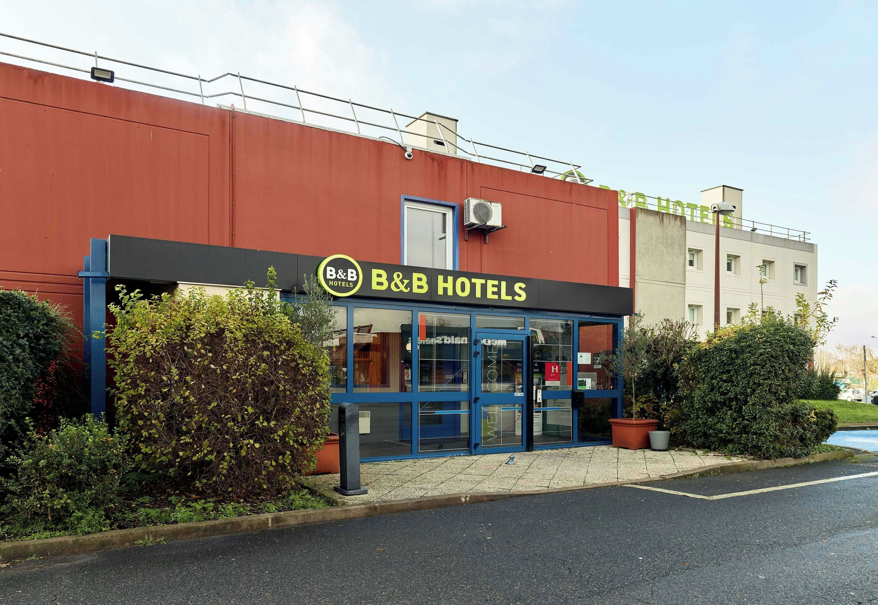 A B&B hotel with a blue facade, a visible entrance, and a parking lot in front.