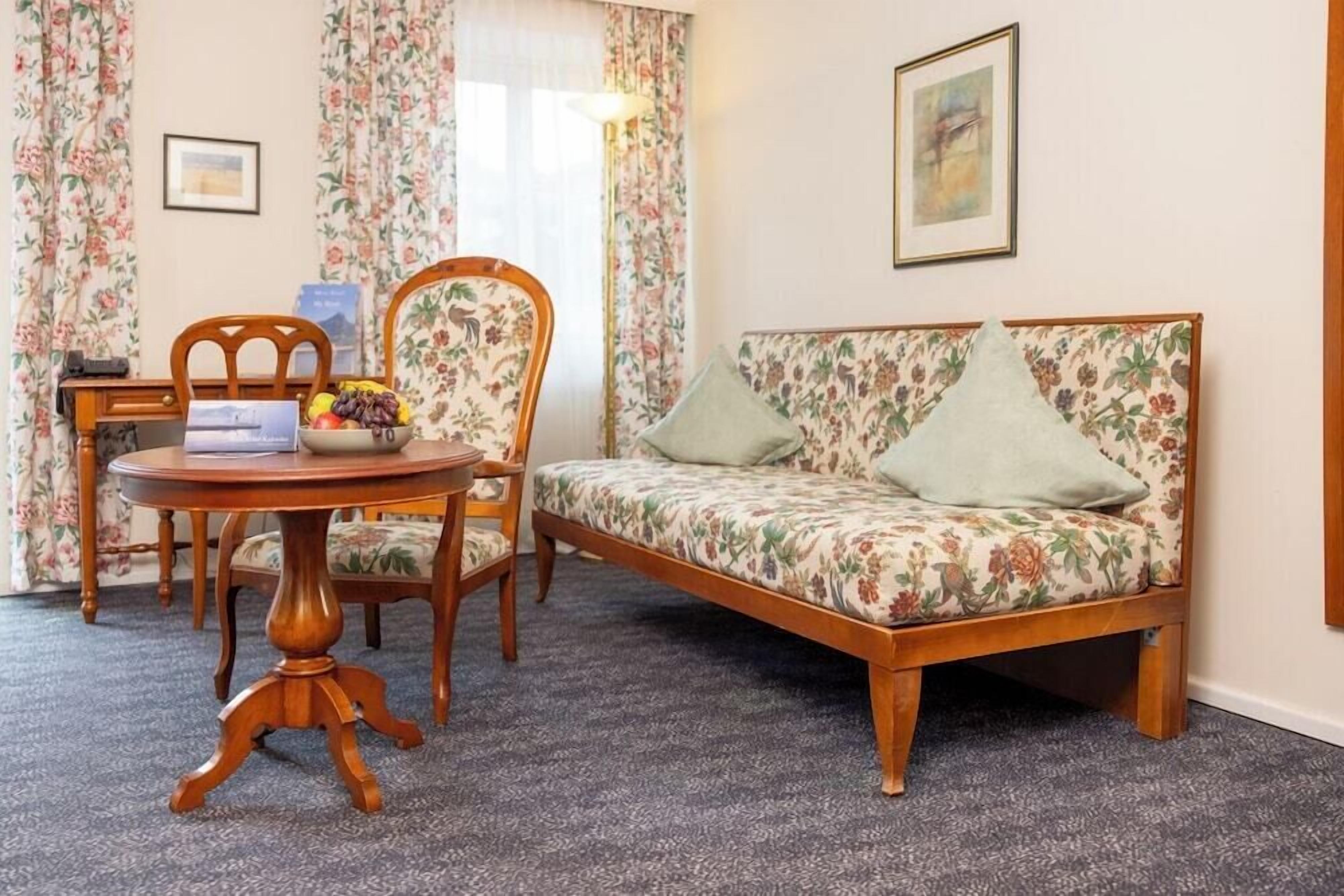 A room with a sofa, chairs, a table with a fruit bowl, and a lamp.