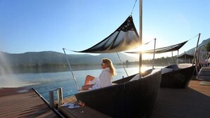 A person relaxing on a wicker chair on a wooden deck overlooking a lake with mountains in the background. - Romantik Hotel Im Weissen Roessl (Sankt Wolfgang im Salzkammergut)